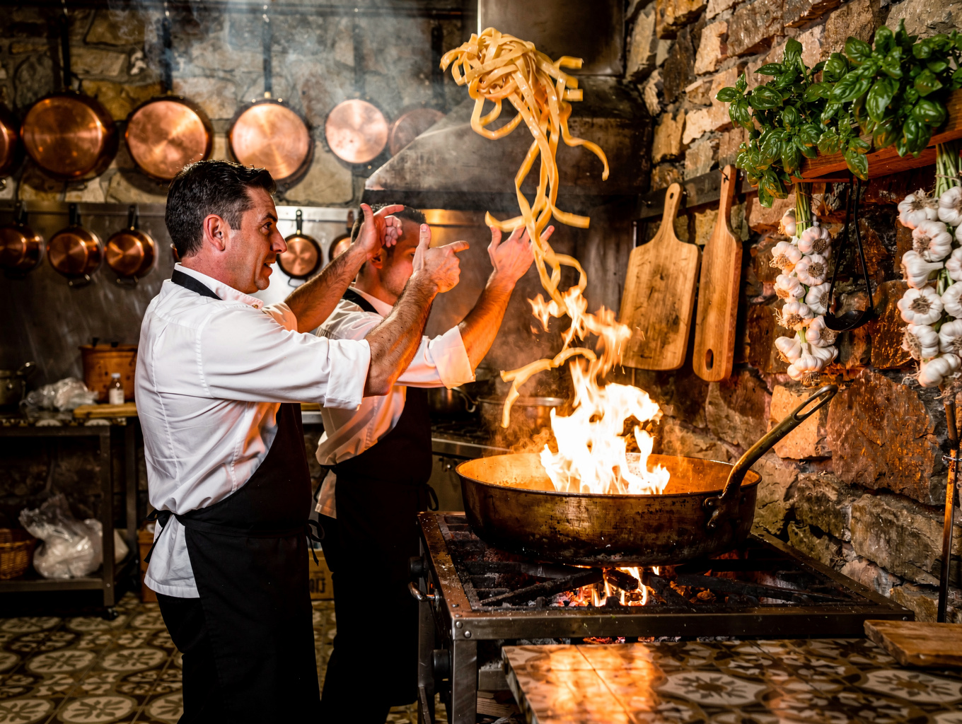 Chefs cooking pasta over an open fire in a modern Italian kitchen